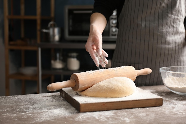 Mulher polvilhando farinha sobre a massa na mesa da cozinha