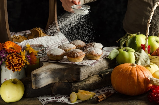 Mulher polvilhe açúcar de confeiteiro em deliciosos muffins de maçã e abóbora caseiros na superfície escura, assados no outono de halloween