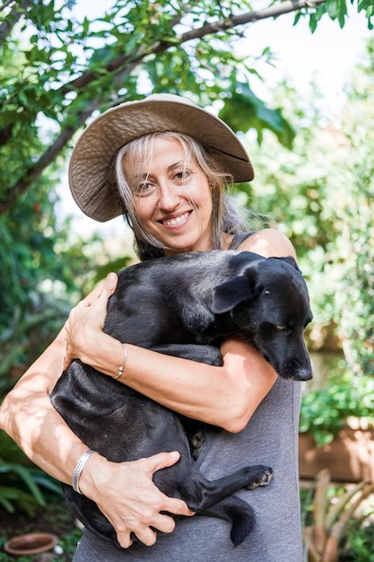 Foto mulher posa com cão preto no jardim em atitude amorosa