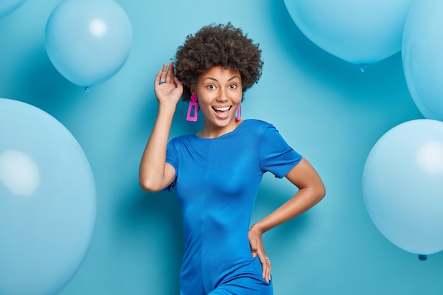 Mulher posa com um vestido da moda sorrindo positivamente e fazendo poses de humor festivo no azul