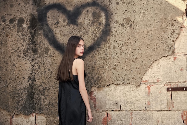 Mulher posando com grafite de coração na parede cinza