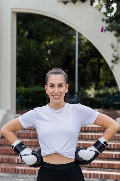 Mulher posando e olhando para a câmera usando luvas de boxe em um parque.