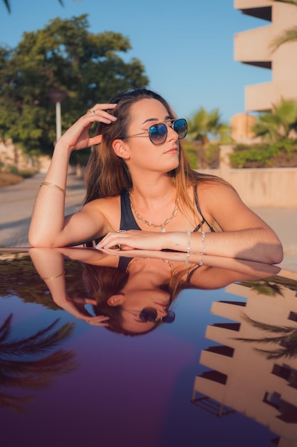 Mulher posando refletida no teto de um carro ao pôr do sol