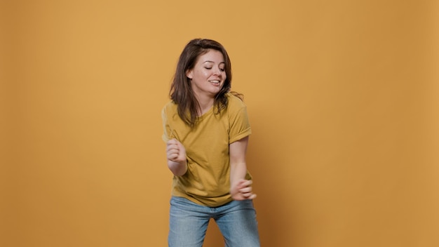 Mulher positiva cheia de energia dançando sozinha no estúdio, sentindo-se confiante, movendo-se ao ritmo da música sobre fundo amarelo. Sorrindo jovem feliz fazendo festa fazendo movimentos de dança peculiares.