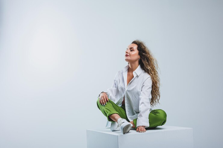 Mulher positiva com cabelo encaracolado em uma camisa branca de algodão leve e calças em um fundo branco isolado Roupa casual feminina