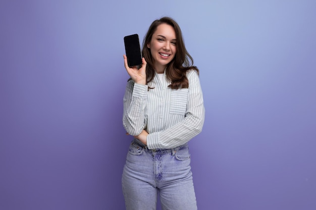 Mulher positiva com cabelo preto em roupas casuais com um telefone nas mãos em um estúdio