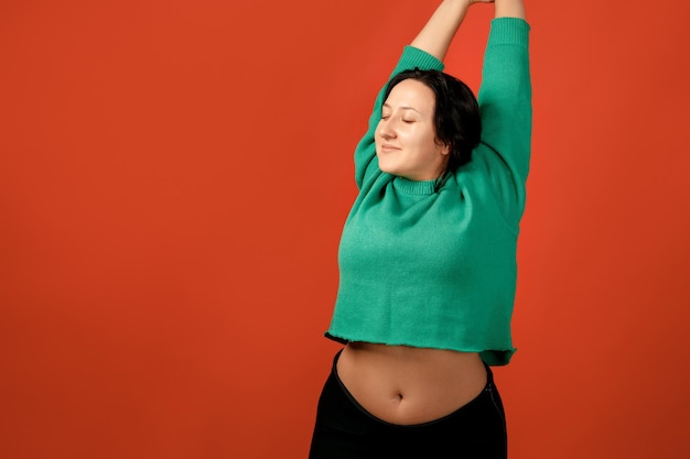 Mulher positiva feliz plus size. conceito positivo de corpo feliz. eu amo meu corpo. mulher atraente com excesso de peso posando na câmera no estúdio em um fundo colorido. garota vestindo um suéter