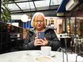 Foto mulher pov sênior olhando para o celular com os cafés já terminados