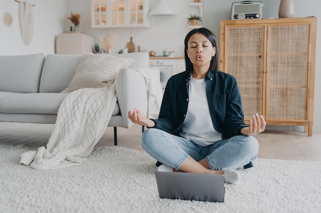 Mulher pratica ioga no laptop respirando profundamente sentada no chão em casa Meditação para alívio do estresse