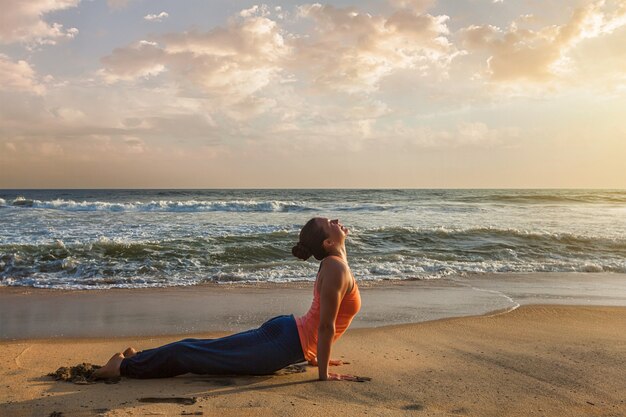 Mulher pratica yoga asana Urdhva Mukha Svanasana na praia