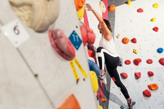 Mulher praticando escalada em parede artificial dentro de casa. Estilo de vida ativo e conceito de boulder.