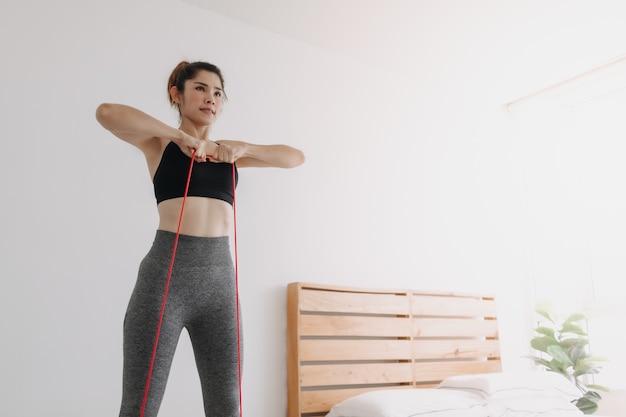 Mulher praticando esportes usa faixa de resistência e treino de linha na vertical no quarto