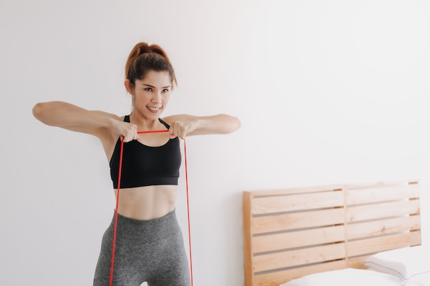 Mulher praticando esportes usa faixa de resistência e treino de linha na vertical no quarto