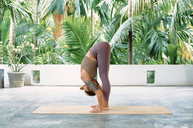 Mulher praticando ioga avançada em uma série de tapete orgânico de poses de ioga fundo tropical