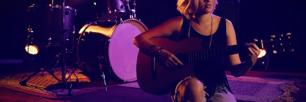 Mulher praticando violão enquanto está sentado no palco