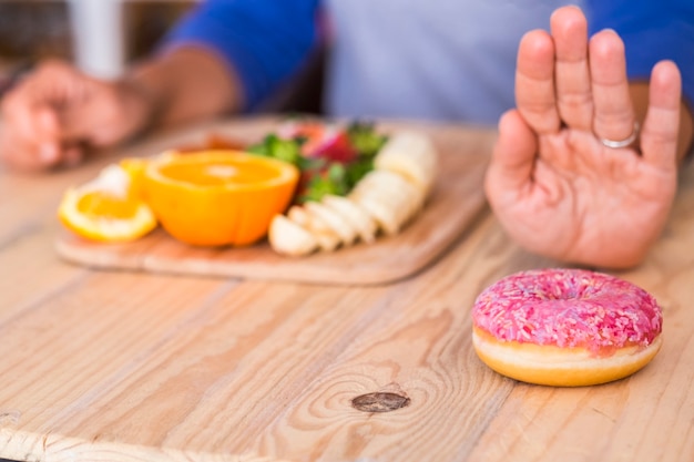 Mulher prefere vegetais e frutas no donut rosa - duas opções - na mesa - em casa interna - estilo de vida e conceito lógicos