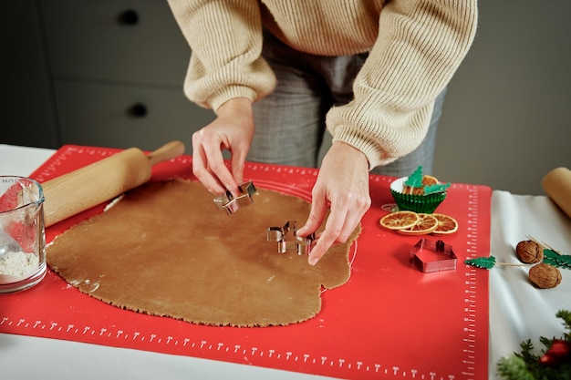 Mulher preparando biscoitos de gengibre na cozinha mãos femininas cortando massa de gengibre com cortador para maki