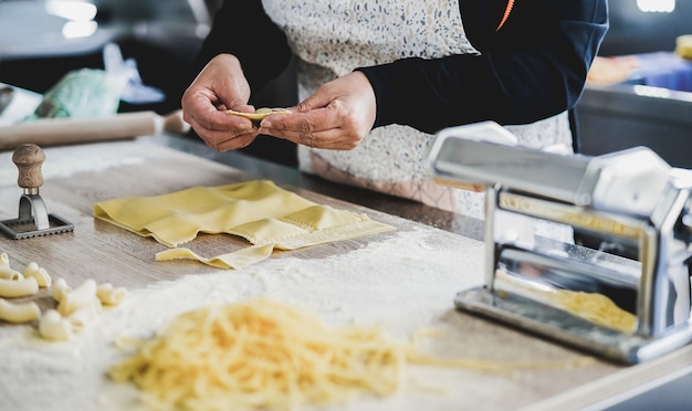 Mulher preparando ravióli fresco dentro da fábrica de macarrão - foco nas mãos