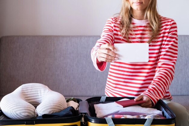 Mulher preparando-se para as férias embalando uma mala na cama mulher segurando um cartão de embarque em branco