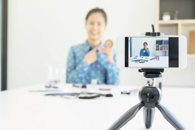 Mulher presente produto de beleza e transmissão de vídeo ao vivo para redes sociais pela internet em casa, conceito de blogueiro de beleza.