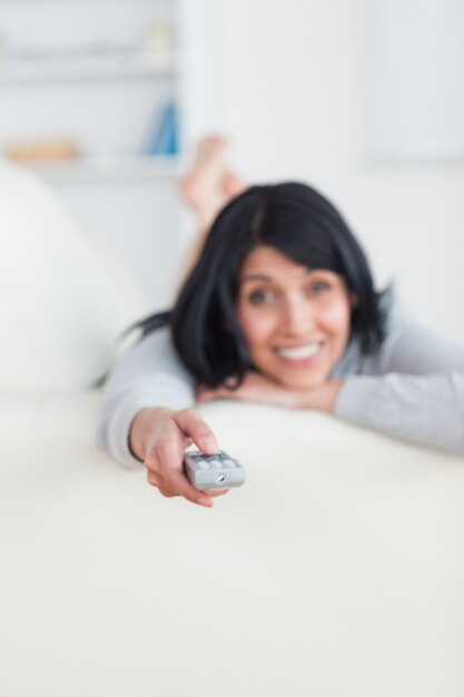 Mulher pressionando um controle remoto enquanto deita no sofá