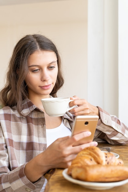 Mulher procurando informações na Internet, usando o celular, durante o café da manhã