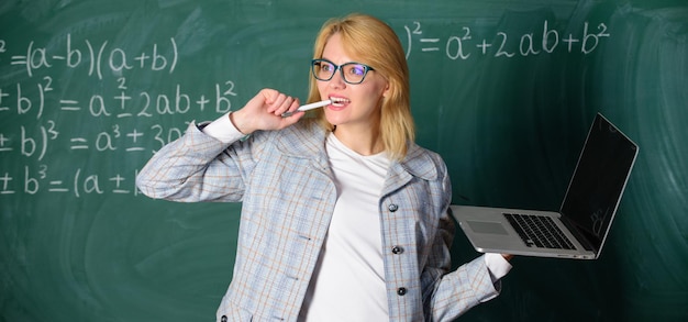 Mulher professora usa óculos segura laptop navegando na internet Educadora inteligente senhora inteligente com laptop moderno surfando na internet fundo de quadro-negro Conceito de tecnologias digitais Ideia em sua mente