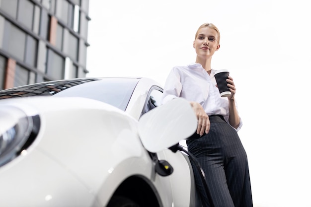 Mulher progressiva com café enquanto carregava carro EV com prédios residenciais