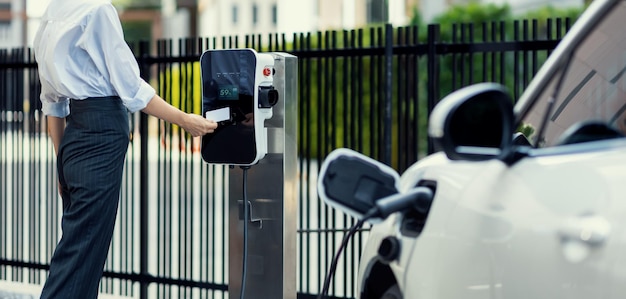 Mulher progressiva paga pelo ponto de carregamento para alimentar o veículo elétrico recarregável