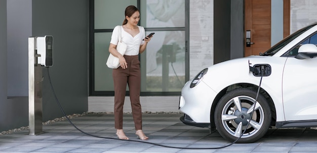 Foto mulher progressiva segurando o telefone na estação de carregamento doméstico ev na garagem