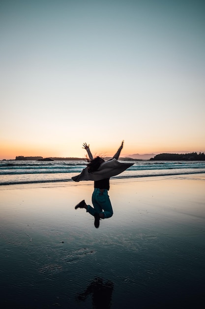 Foto mulher pulando na praia contra o céu durante o pôr do sol