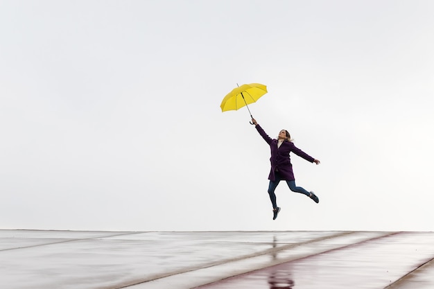 Mulher pulando no horizonte com um guarda-chuva amarelo em um dia chuvoso.