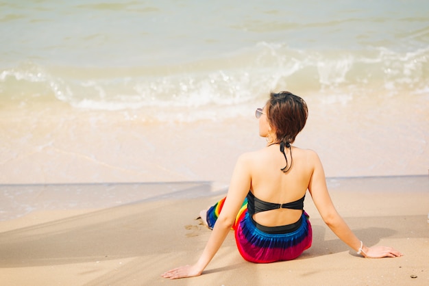 Mulher que aprecia a praia que relaxa alegre no verão pela água azul tropical.