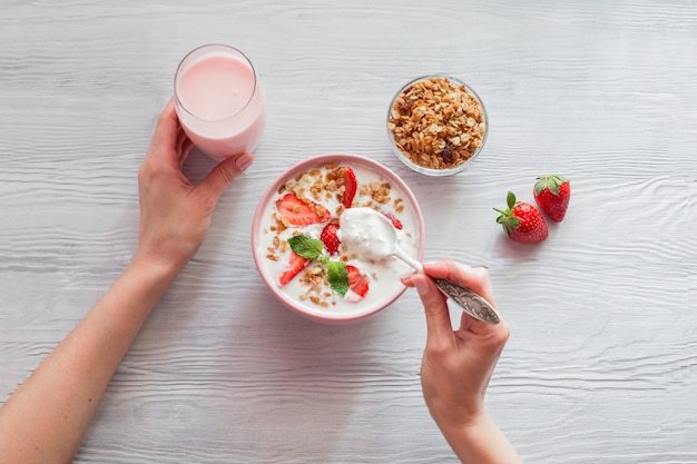 Mulher que come um iogurte saudável com muesli e morangos