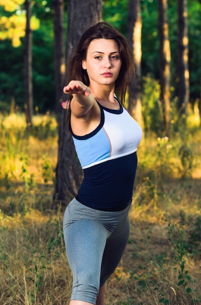 Mulher que está na pose do guerreiro na paisagem da floresta. Fechar-se