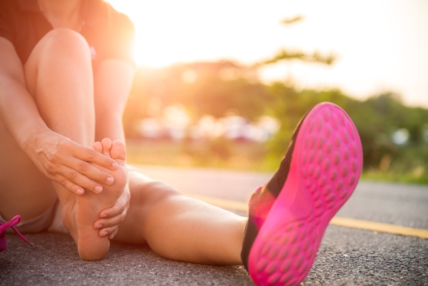 Mulher que sofre de uma lesão no tornozelo durante o exercício, cuidados de saúde e conceito do esporte.