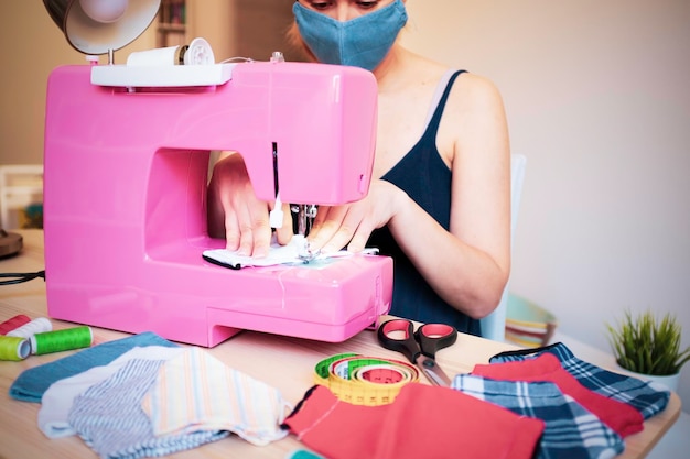 Mulher que trabalha com máquina de costura fazendo máscara médica facial moderna para prevenir e impedir a propagação do coronavírus Conceito de fabricação caseira Reutilização de roupas usadas Foco principal nas mãos