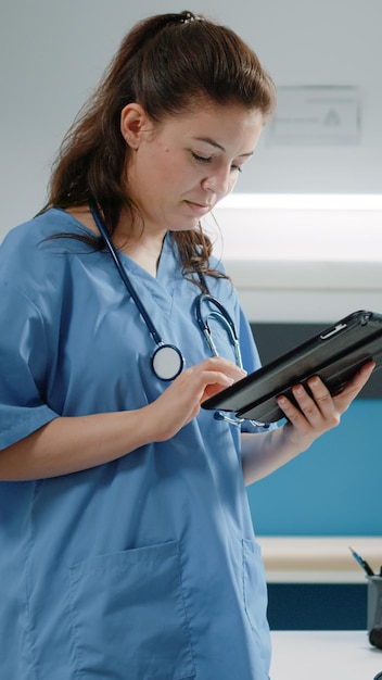 Mulher que trabalha como enfermeira e segurando o tablet digital para visita de verificação no gabinete. assistente médico usando tecnologia e dispositivo moderno para consulta médica e tratamento de cura.