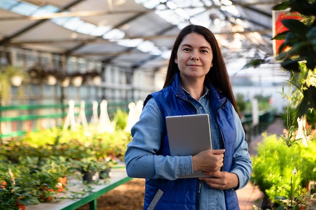 Mulher que trabalha em estufa verificando plantas com tablet