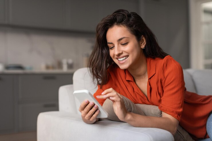 Foto mulher radiante enviando mensagens de texto no smartphone sentada no sofá