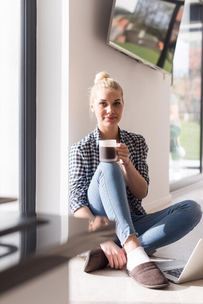 Mulher real usando laptop em casa no chão bebendo café desfrutando de relaxamento