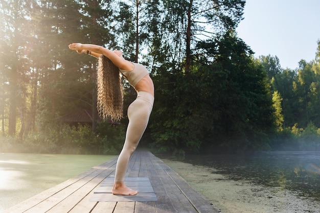 mulher realiza um exercício de curvatura nas costas Hasta Uttanasana pose fica em uma ponte de madeira