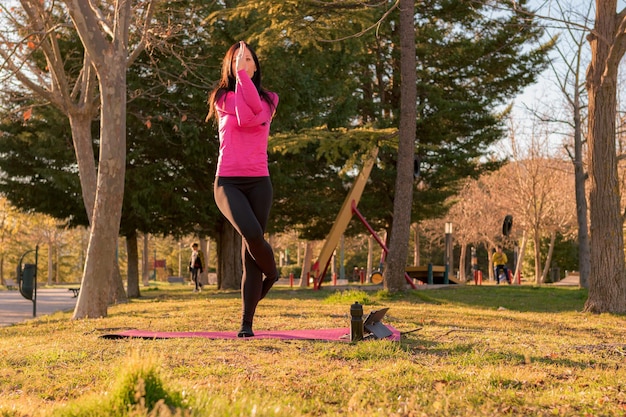Mulher realizando exercícios de ioga em um parque ao pôr do sol