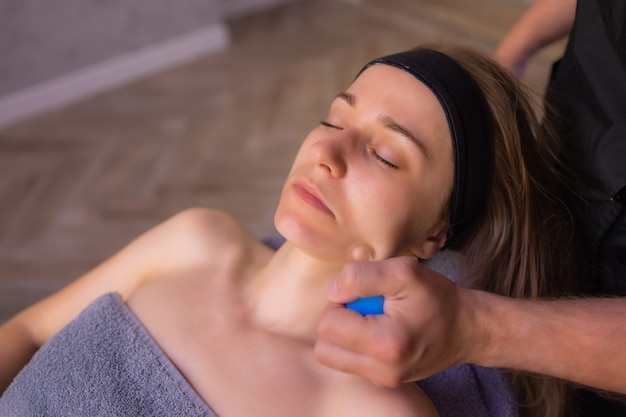 Mulher recebe massagem facial de rejuvenescimento facial no spa de bem-estar de acupuntura.