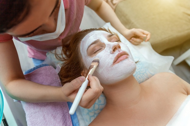 Mulher recebendo tratamento facial com creme nutritivo branco em salão de spa