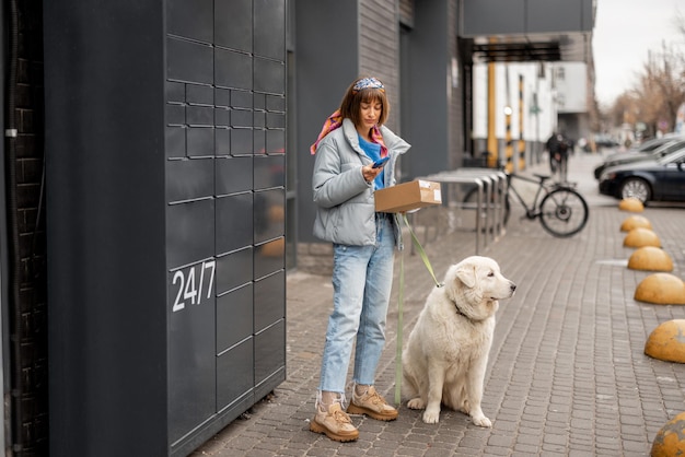 Mulher recebendo um pacote da máquina postal automática durante uma caminhada com seu cachorro