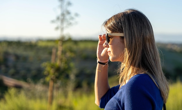 Foto mulher relaxada com óculos de sol olhando para longe enquanto está de pé ao ar livre na natureza