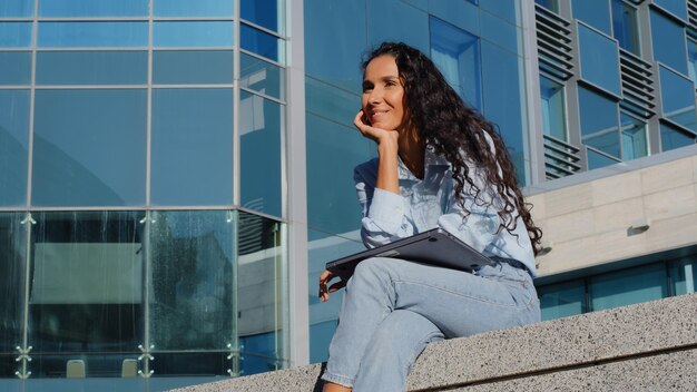 Mulher relaxada de negócios terminando o trabalho online estudando com computador sentado na cidade ao ar livre menina