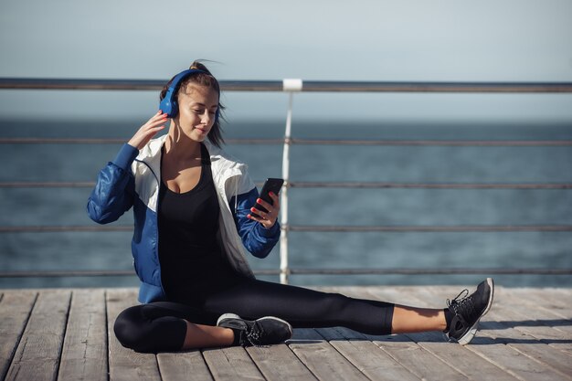 Mulher relaxada em roupas esportivas com fones de ouvido escolhe música em um smartphone para treinar