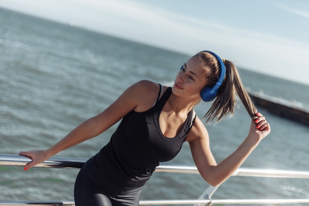 Mulher relaxada em roupas esportivas com fones de ouvido ouve música na praia em um dia ensolarado